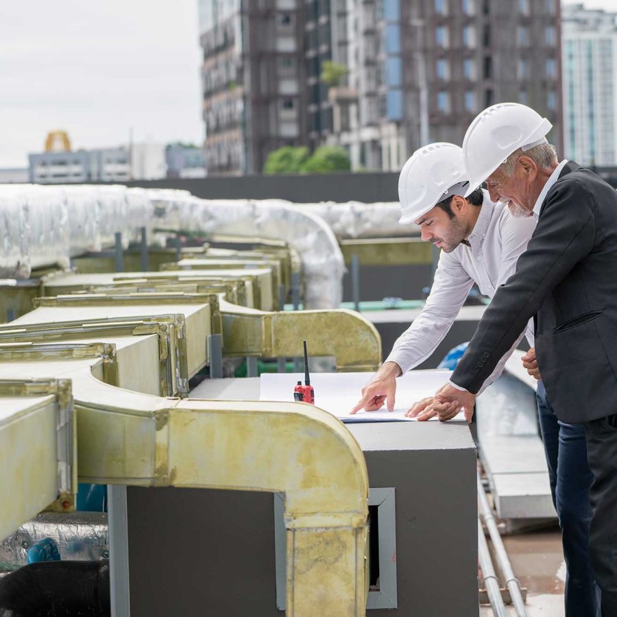 Two construction workers in hard hats review a blueprint together at a building site